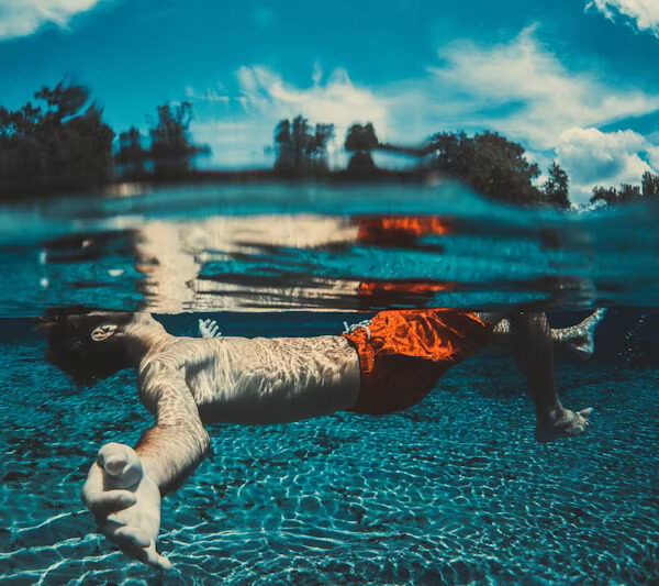 A swimmer floating face-down in clear water, arms stretched forward